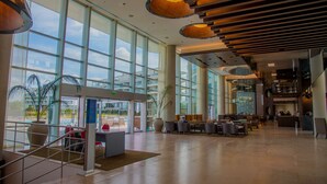 Eine großzügige Lobby mit großen Fenstern, einem Empfangstresen, Sitzbereichen und einer Treppe.
