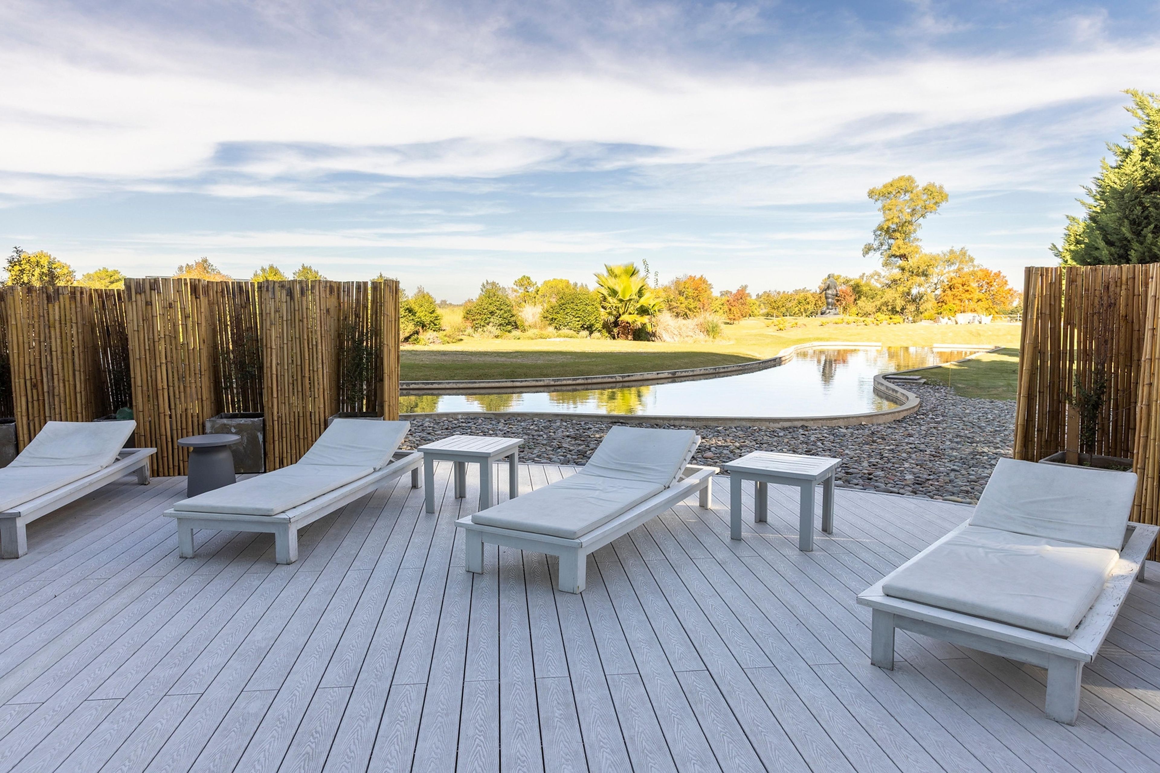 A deck with lounge chairs and tables overlooking a pond and a golf course.