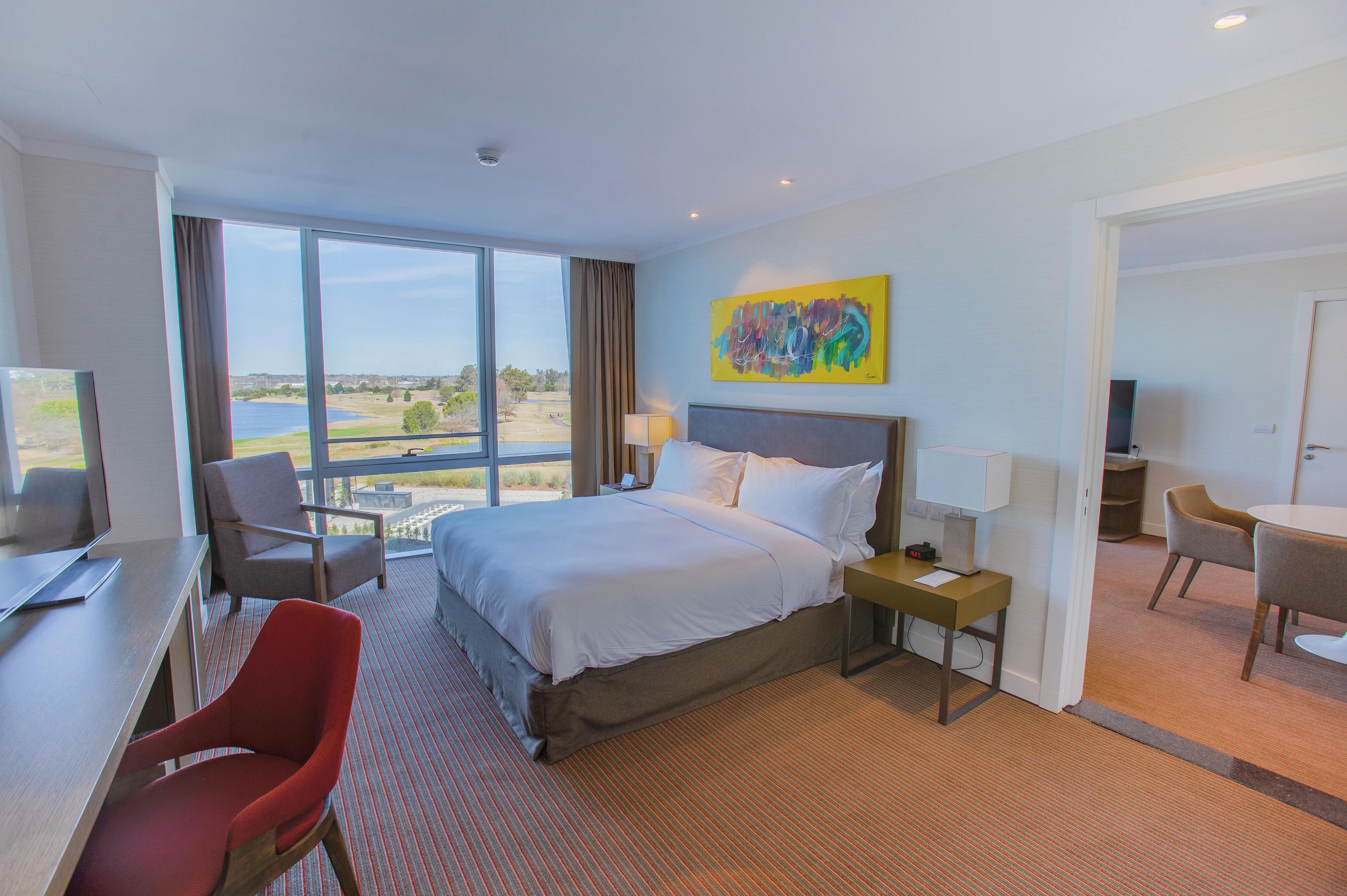 A hotel room with a large bed, a desk, a chair, a TV, and a painting on the wall.