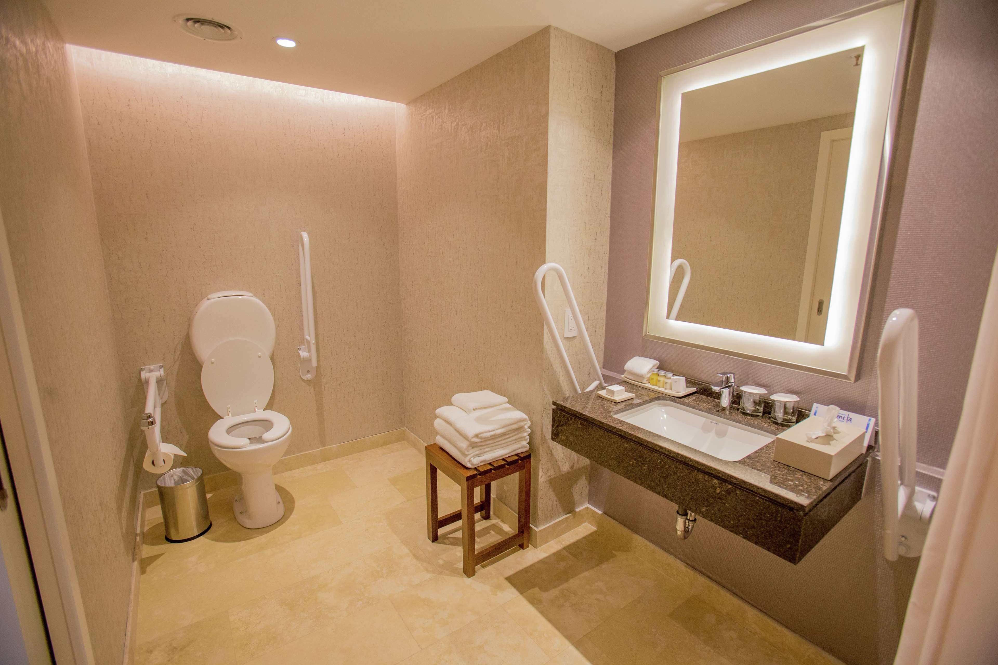 A bathroom with a toilet, sink, mirror, and a small wooden stool with towels.