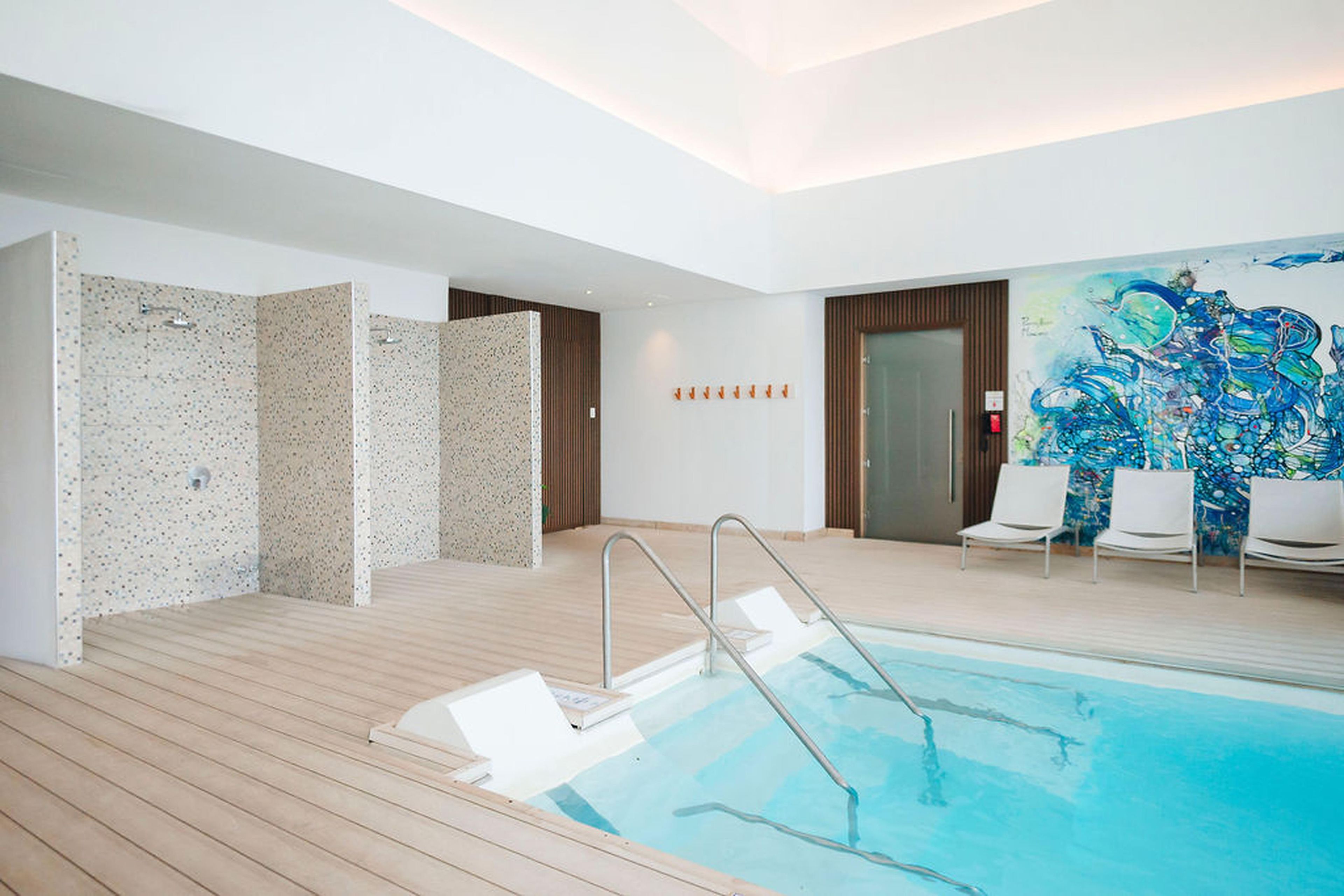 Une piscine intérieure moderne dotée d’une terrasse en bois, d’un mur en verre et d’une fresque murale abstraite aux couleurs vives.