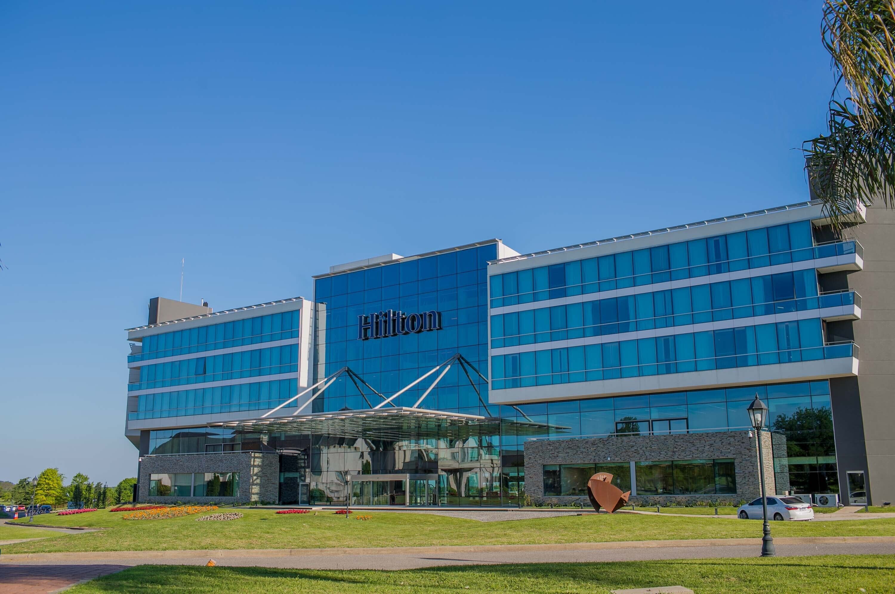 Un hotel Hilton moderno con fachada de vidrio, varios pisos y una entrada distintiva con una cubierta de cristal.