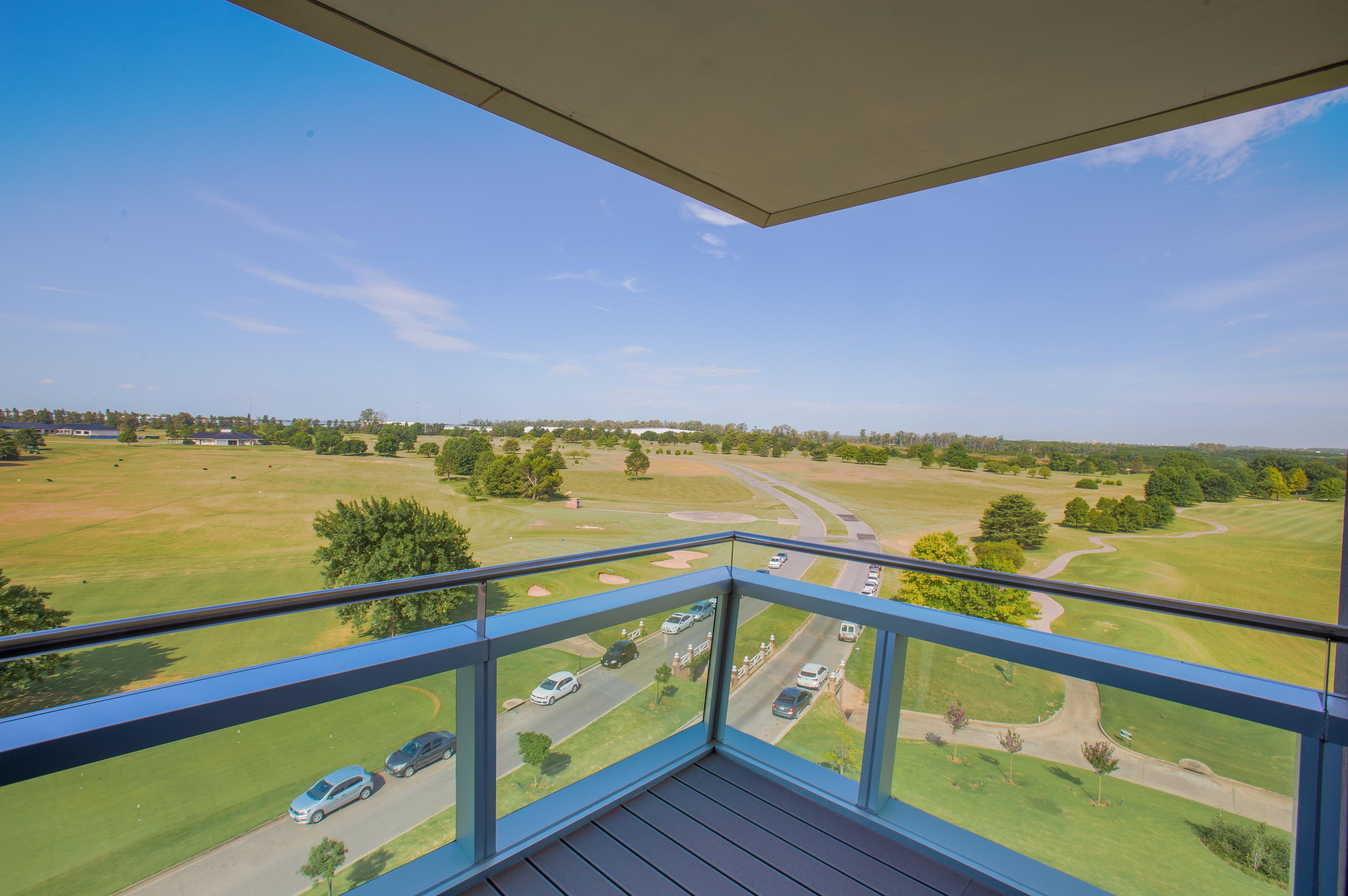 A balcony with a view of a golf course and a road with cars.