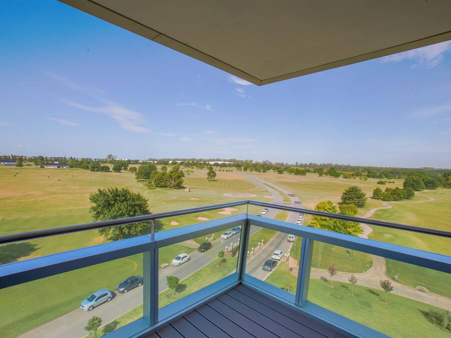 En balkon med udsigt over en golfbane og en vej med biler.