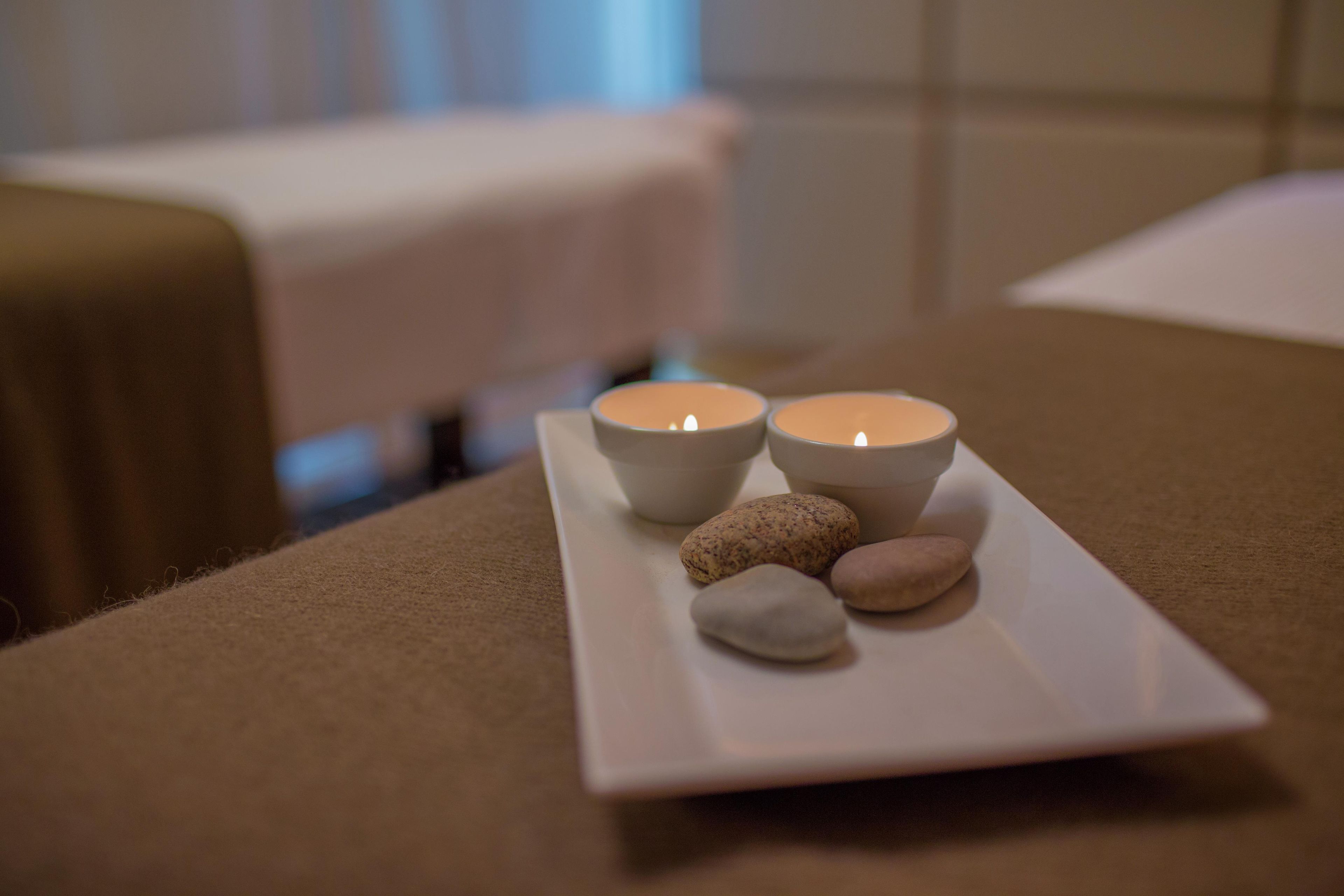 A table with two candles and three smooth stones on a white tray.