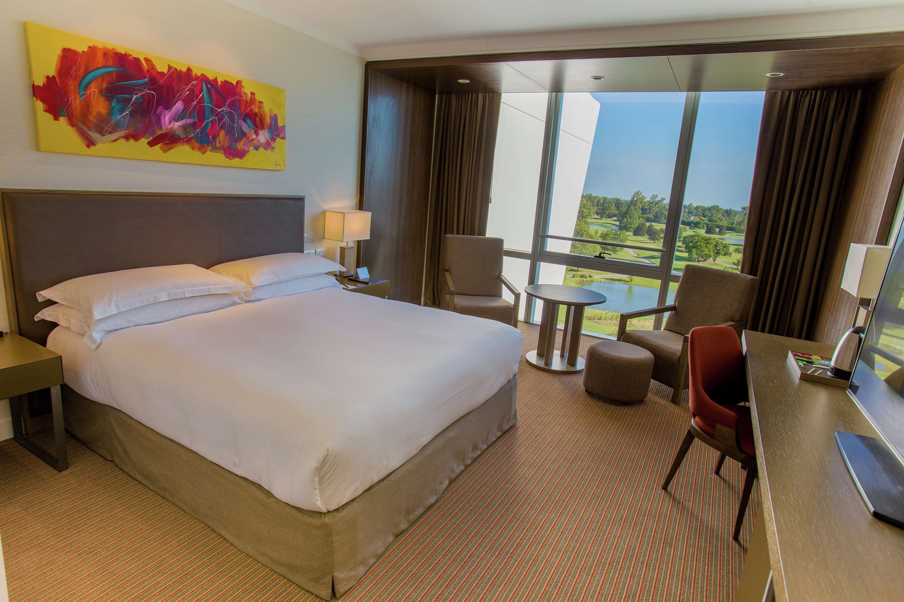 Habitación de hotel con una cama grande, un escritorio, una silla y vista a un campo de golf.