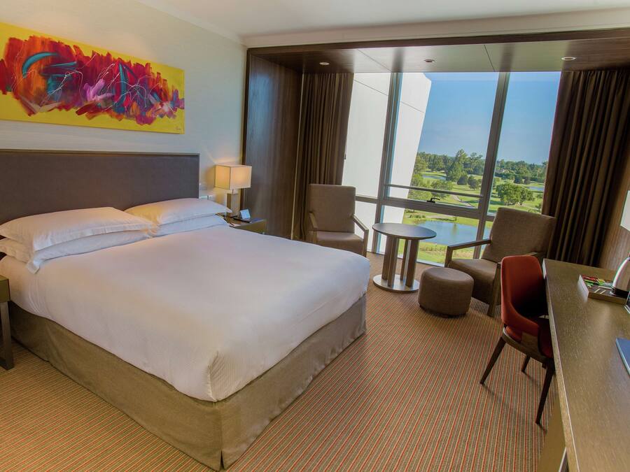 Habitación de hotel con una cama grande, un escritorio, una silla y vista a un campo de golf.
