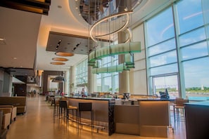 A modern hotel lobby with a curved staircase, large windows, and a bar area. - Hilton Pilar (Fátima)