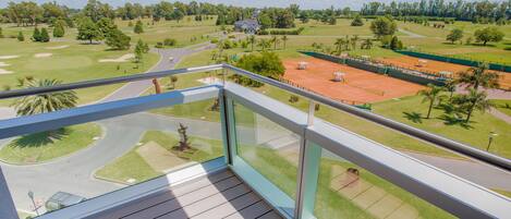 A balcony with a view of a golf course, a tennis court, and a residential area.