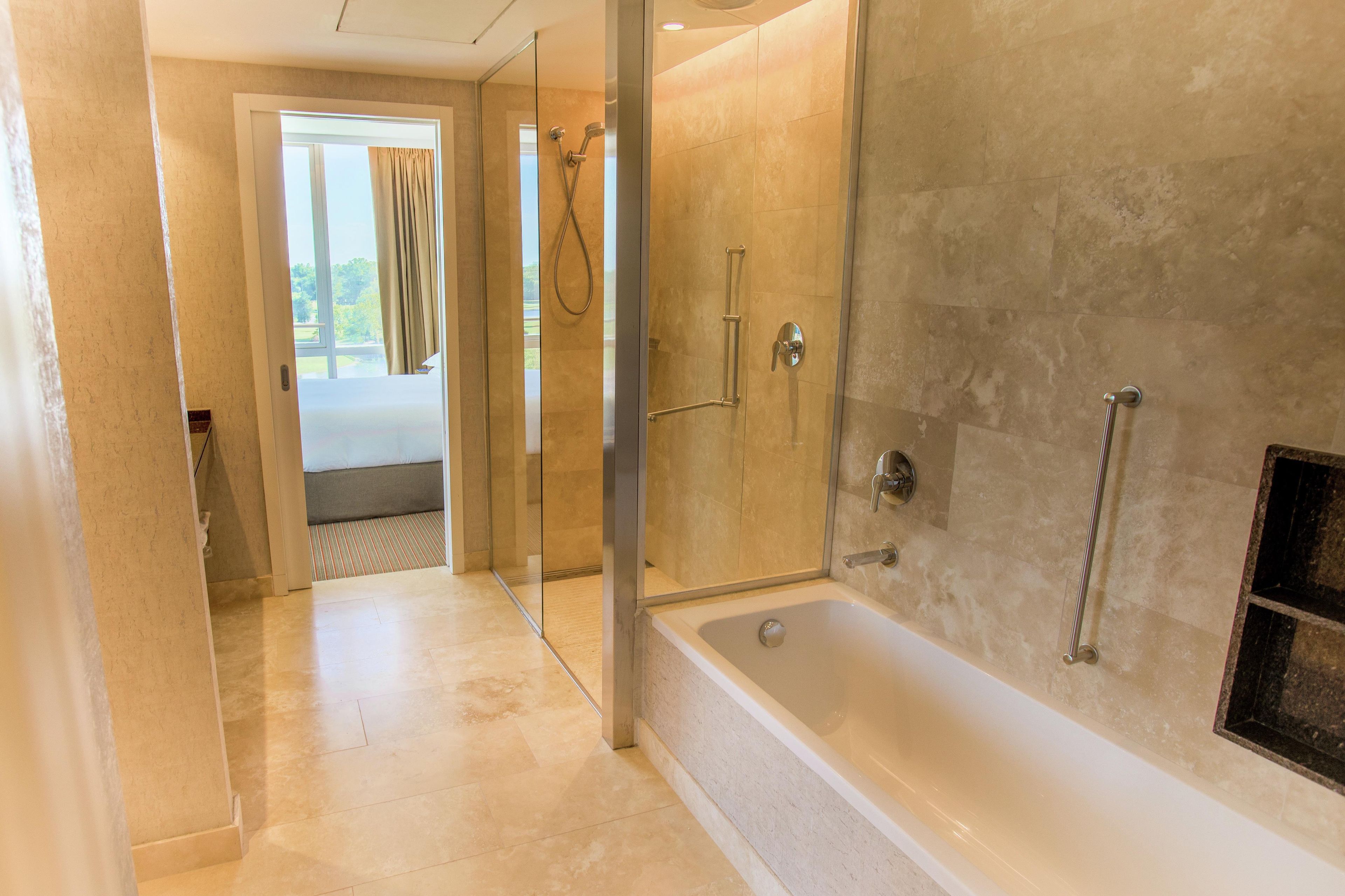 A modern bathroom with a glass-enclosed shower, a bathtub, and a visible outdoor view through a door.