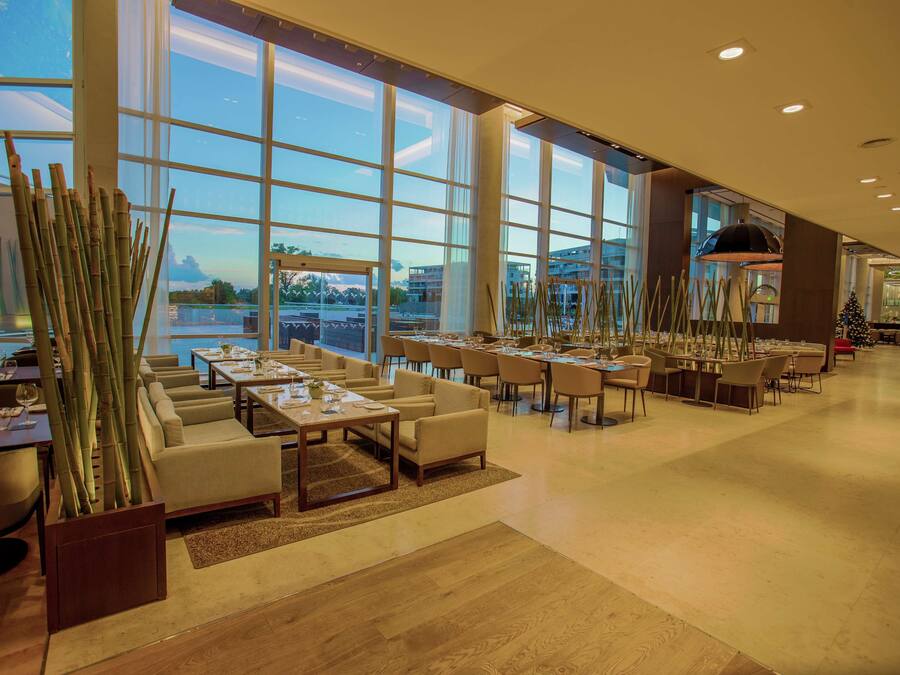 A spacious restaurant with large windows, modern furniture, and a view of the cityscape.