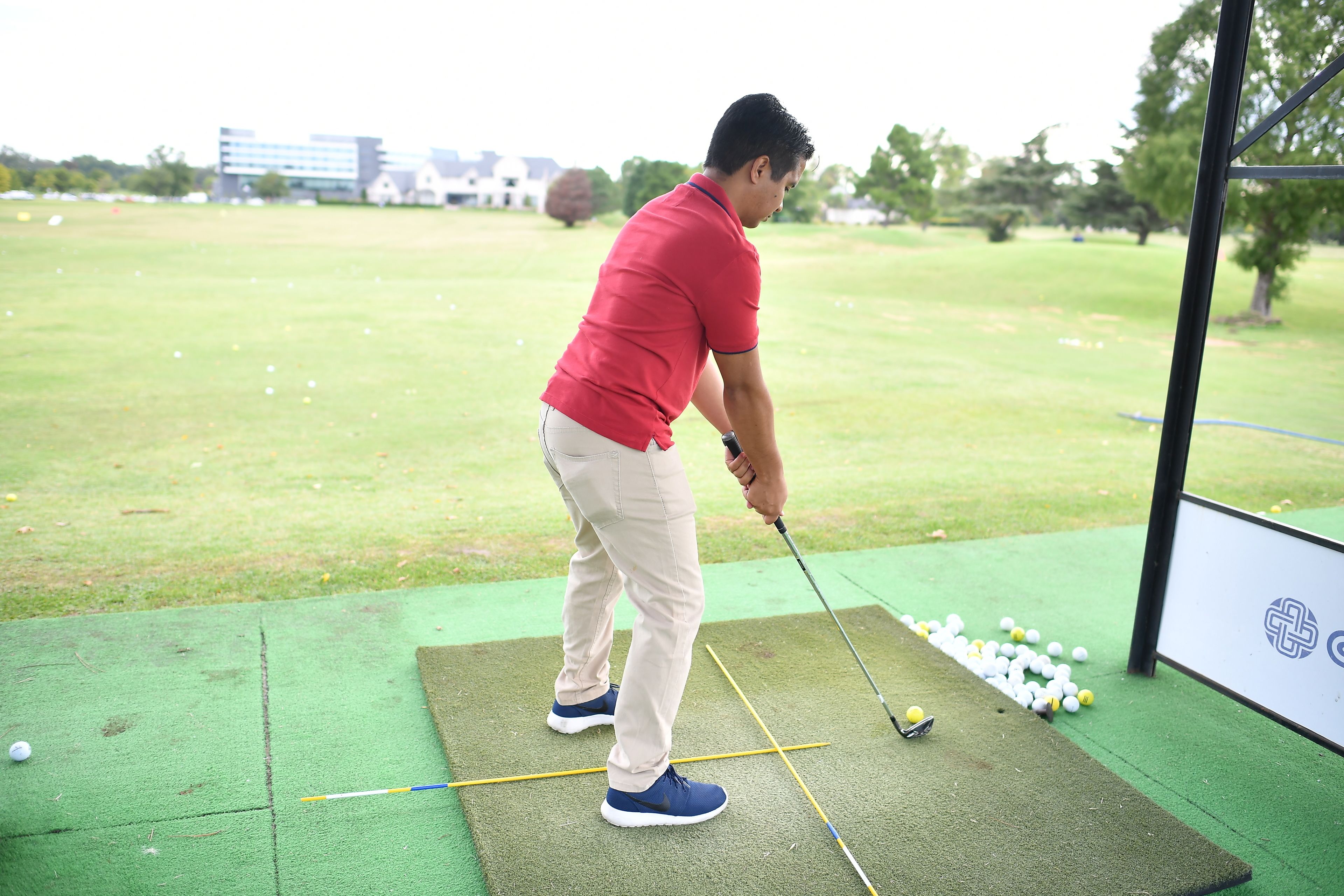 Una persona practicando golf sobre una esterilla verde, con una pelota y palos.