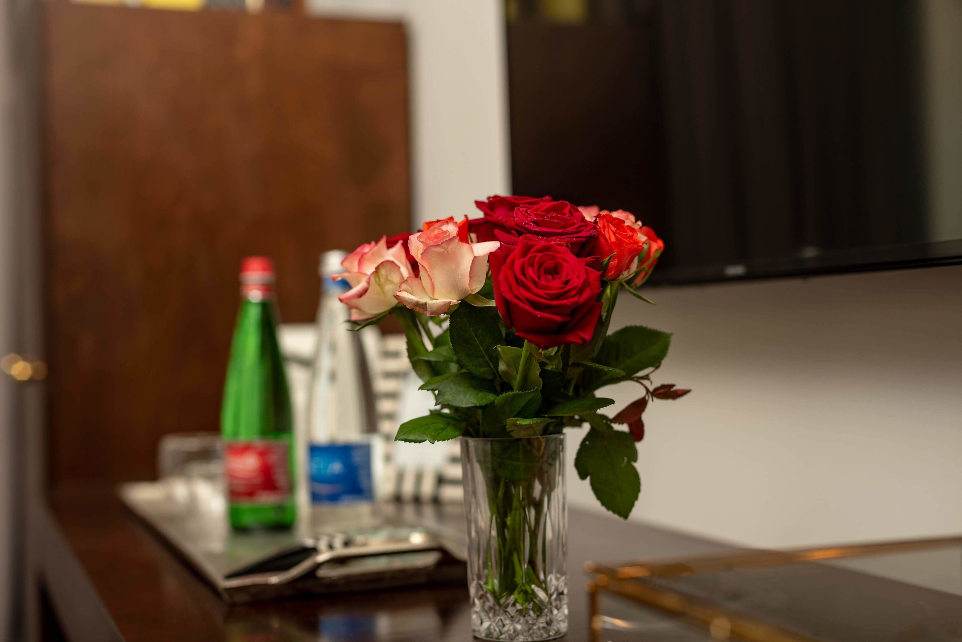 Un vase en verre contenant des roses rouges et roses, posé sur une table en bois.