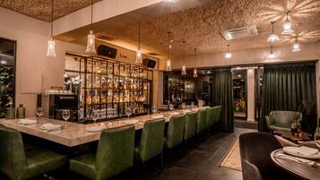 A bar area with a long counter, green upholstered chairs, and pendant lighting.