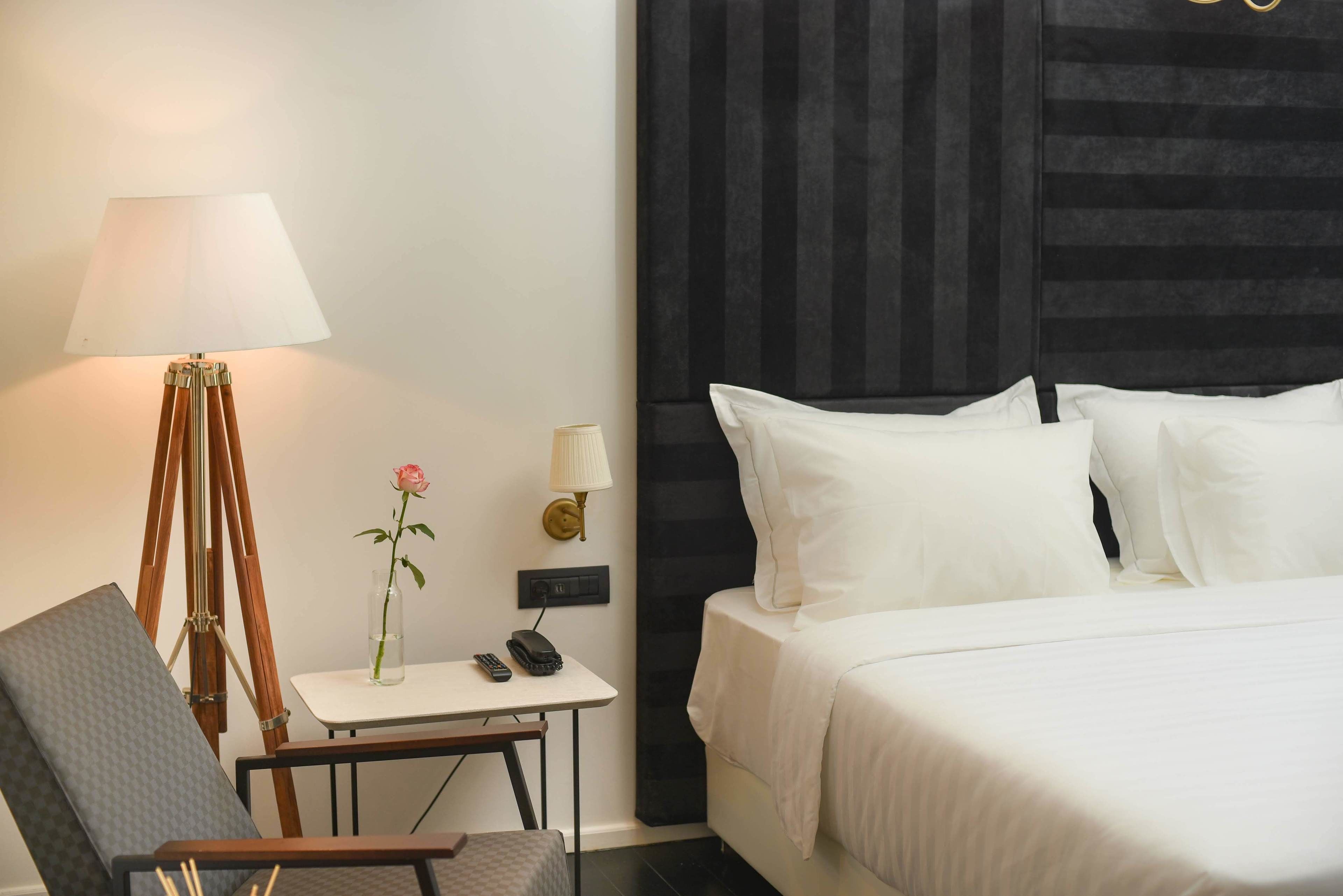 Habitació d'hotel amb llit, escriptori amb làmpada, cadira i gerra amb una flor.