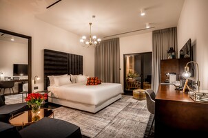 Una habitación de hotel moderna con una cama grande, un escritorio, una silla, una mesita de centro y un jarrón de flores.