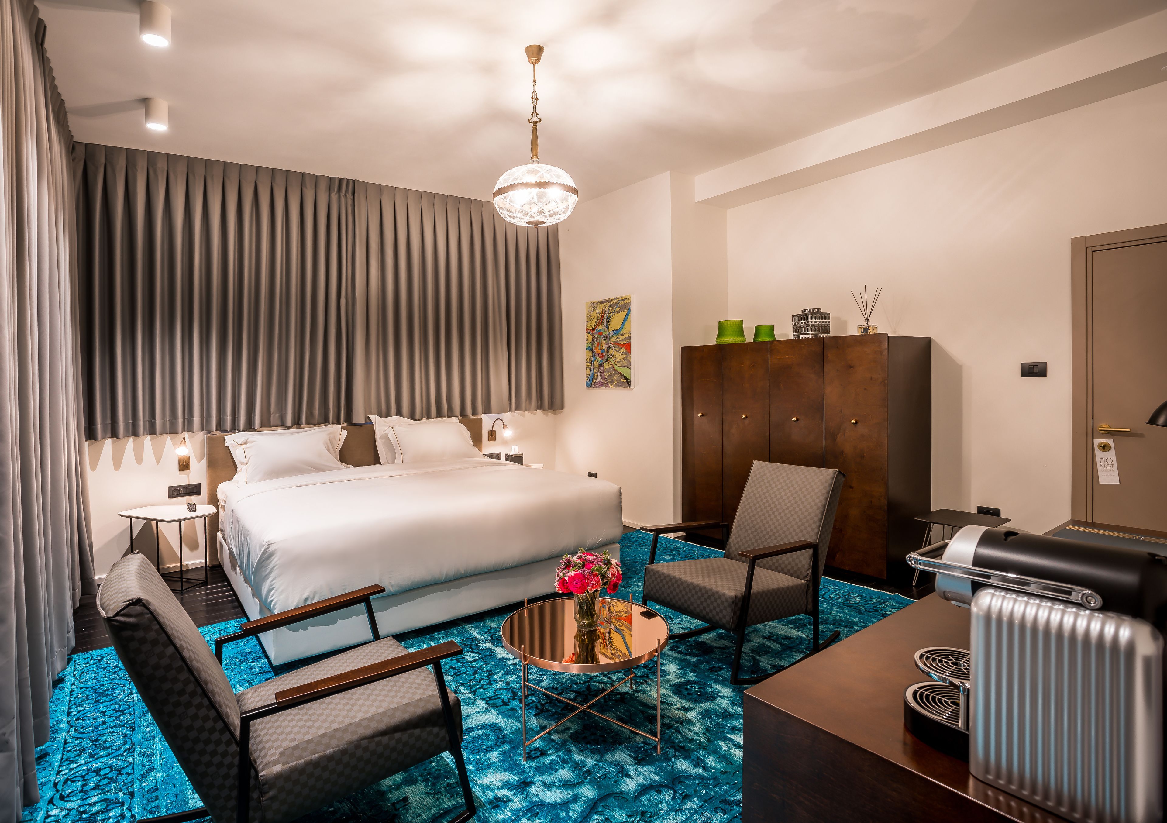 Habitación de hotel con una cama grande, un área de estar con una mesa de centro, un sofá, una silla, un escritorio y un radiador.
