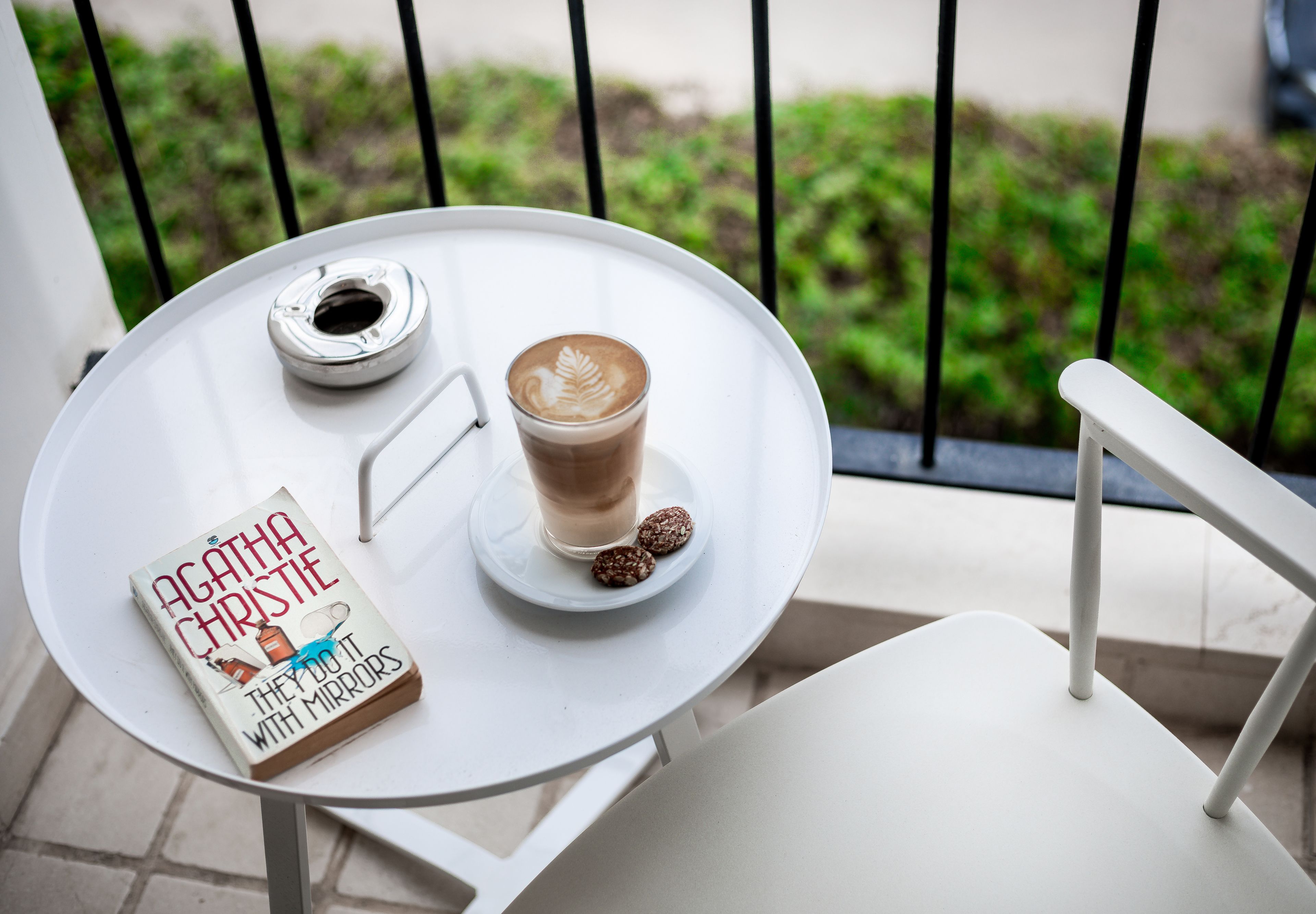 Ett vitt bord med en bok, en kopp kaffe och två kakor på en balkong.