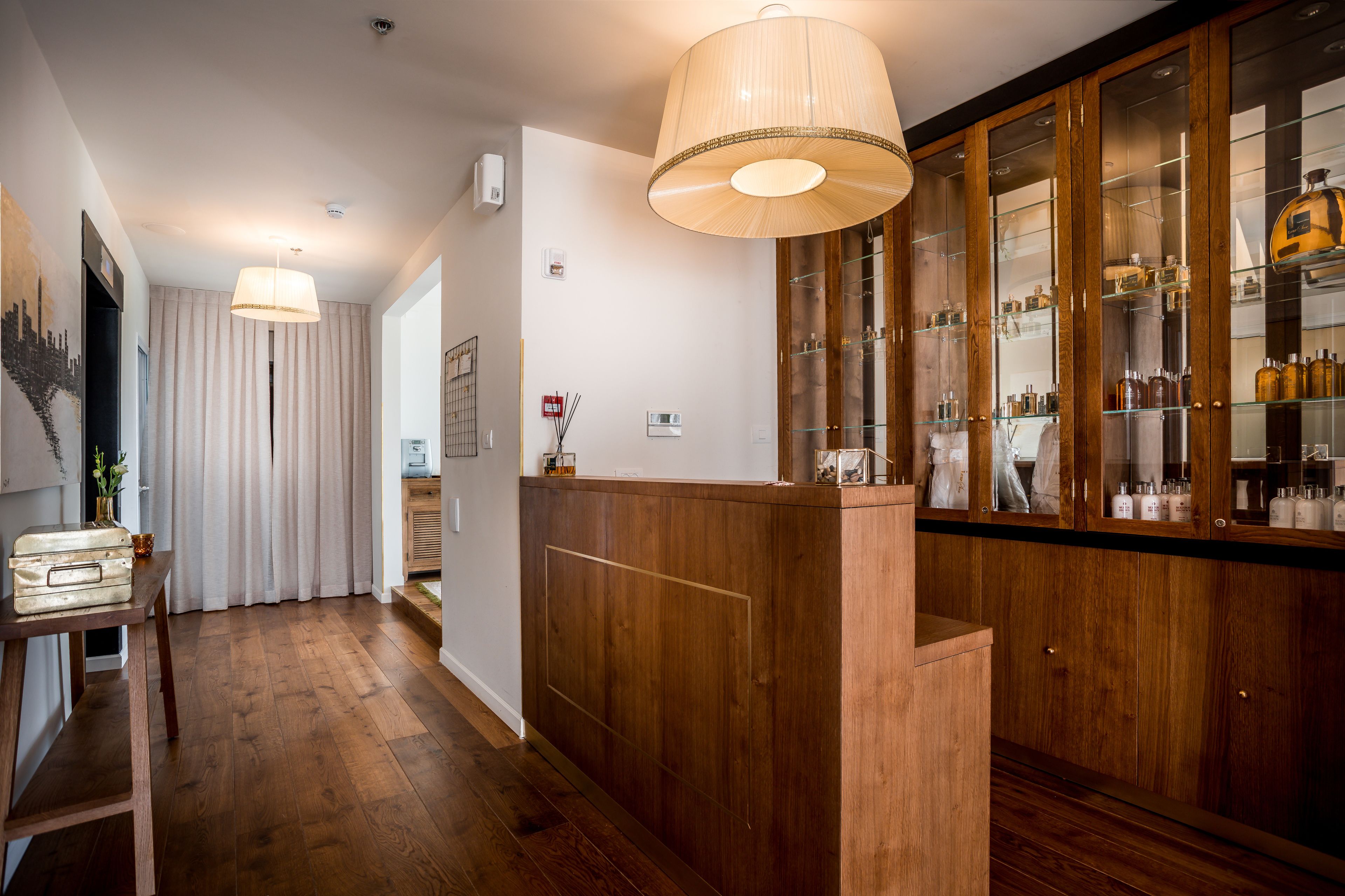 Un vestíbulo de hotel con suelo de madera, una recepción, un amplio expositor de vidrio y una lámpara colgante.