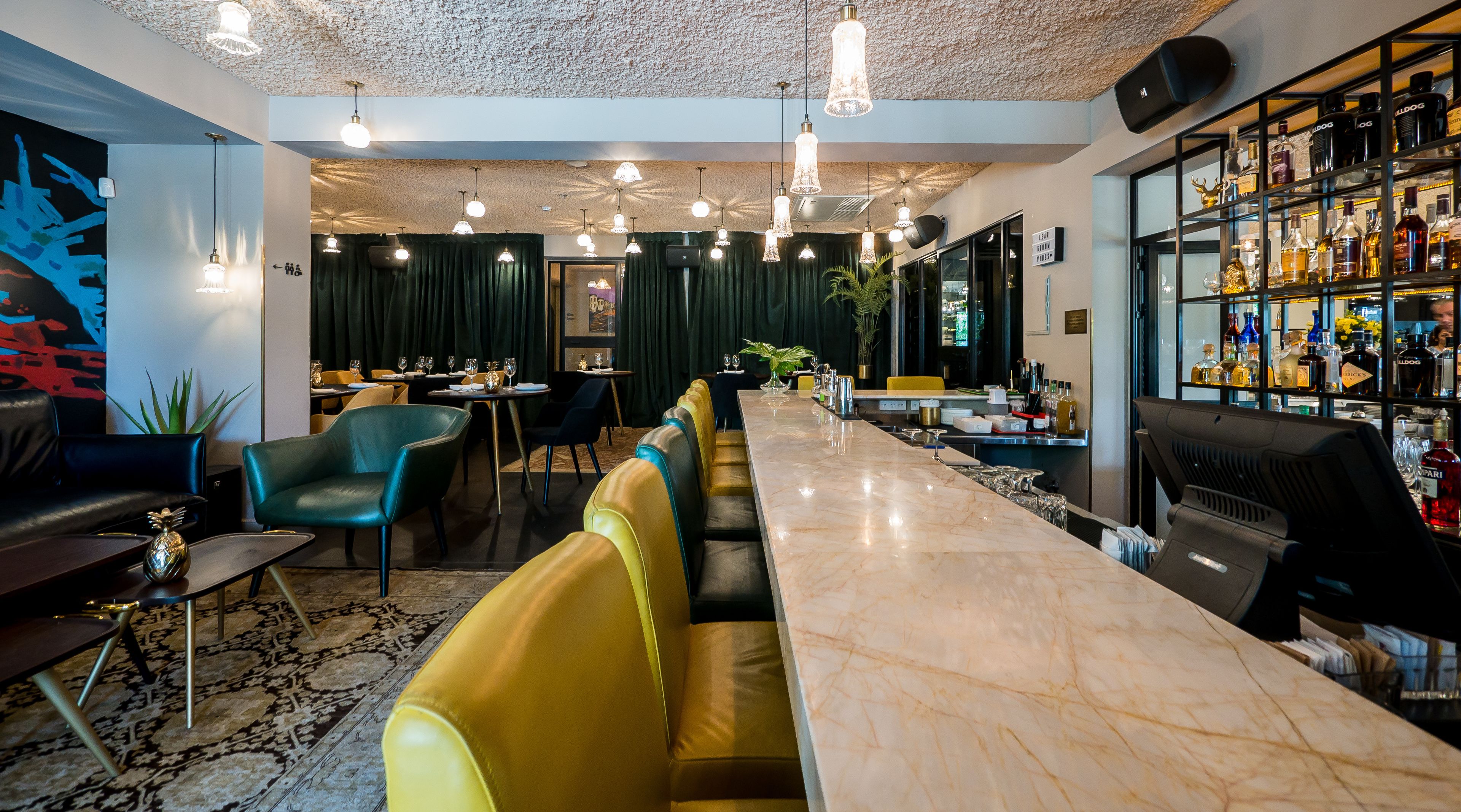 Zona de bar con mostrador de mármol, asientos de cuero y una variedad de botellas.