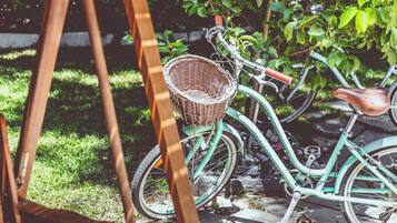 Ein altes Fahrrad mit einem Korbwannenaufsatz und einem Ledersitz, abgestellt auf befestigter Strecke, im Hintergrund Grün.