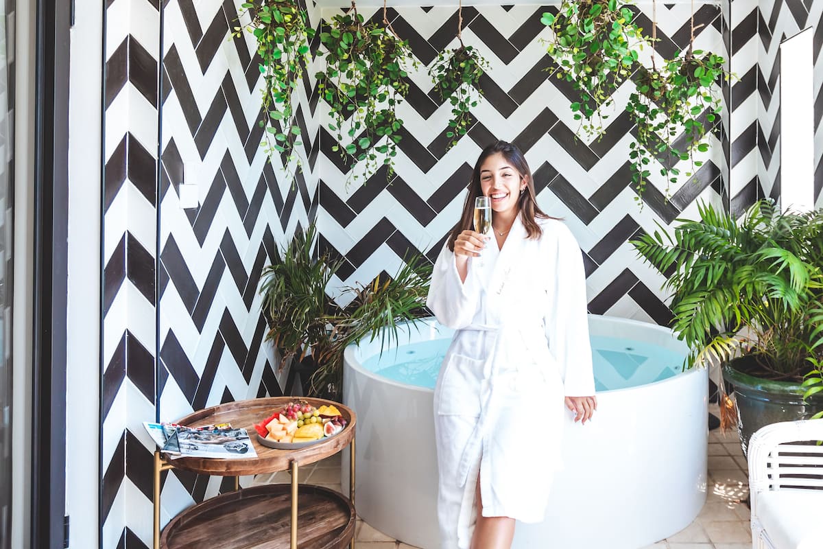 A modern outdoor area with a black and white chevron-patterned wall, a hot tub, and a table with fruits and magazines.