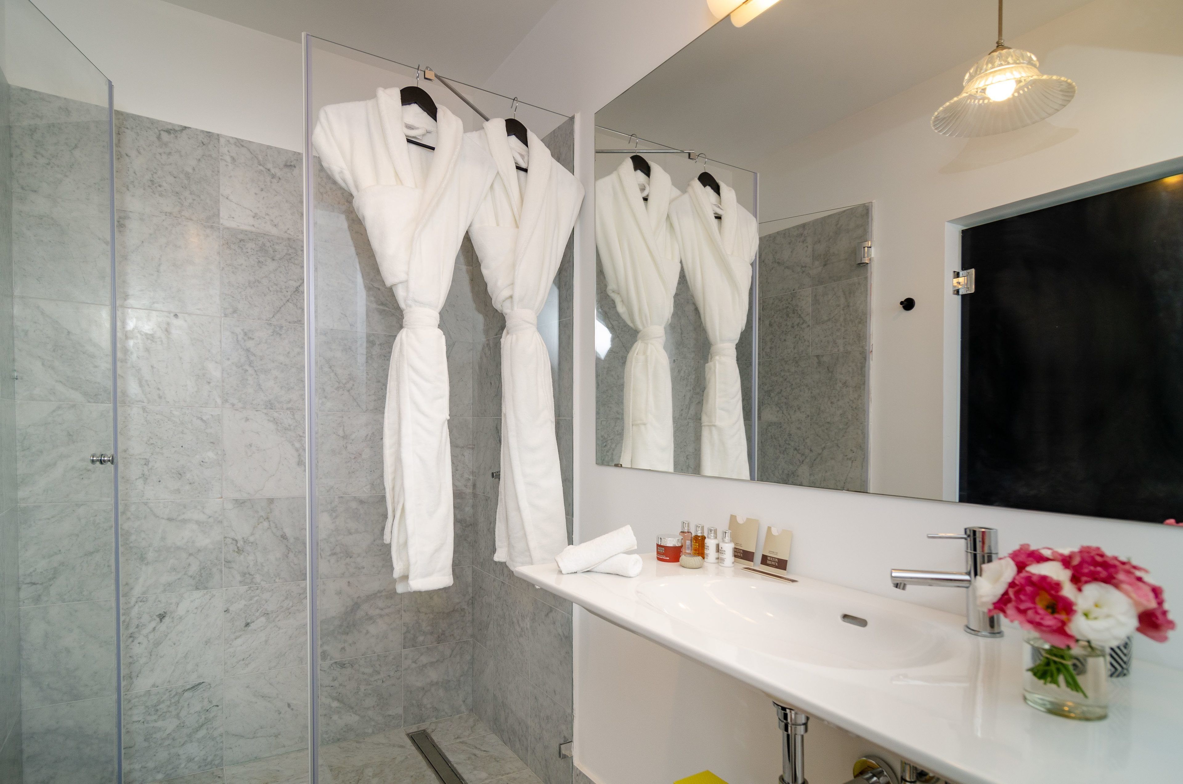 Un baño moderno con cabina de ducha de vidrio, un lavabo blanco con artículos de aseo y un espejo grande.