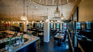 Un restaurante con varias áreas de comedor, candelabros de cristal colgantes y una zona de bar con un jarrón de flores.
