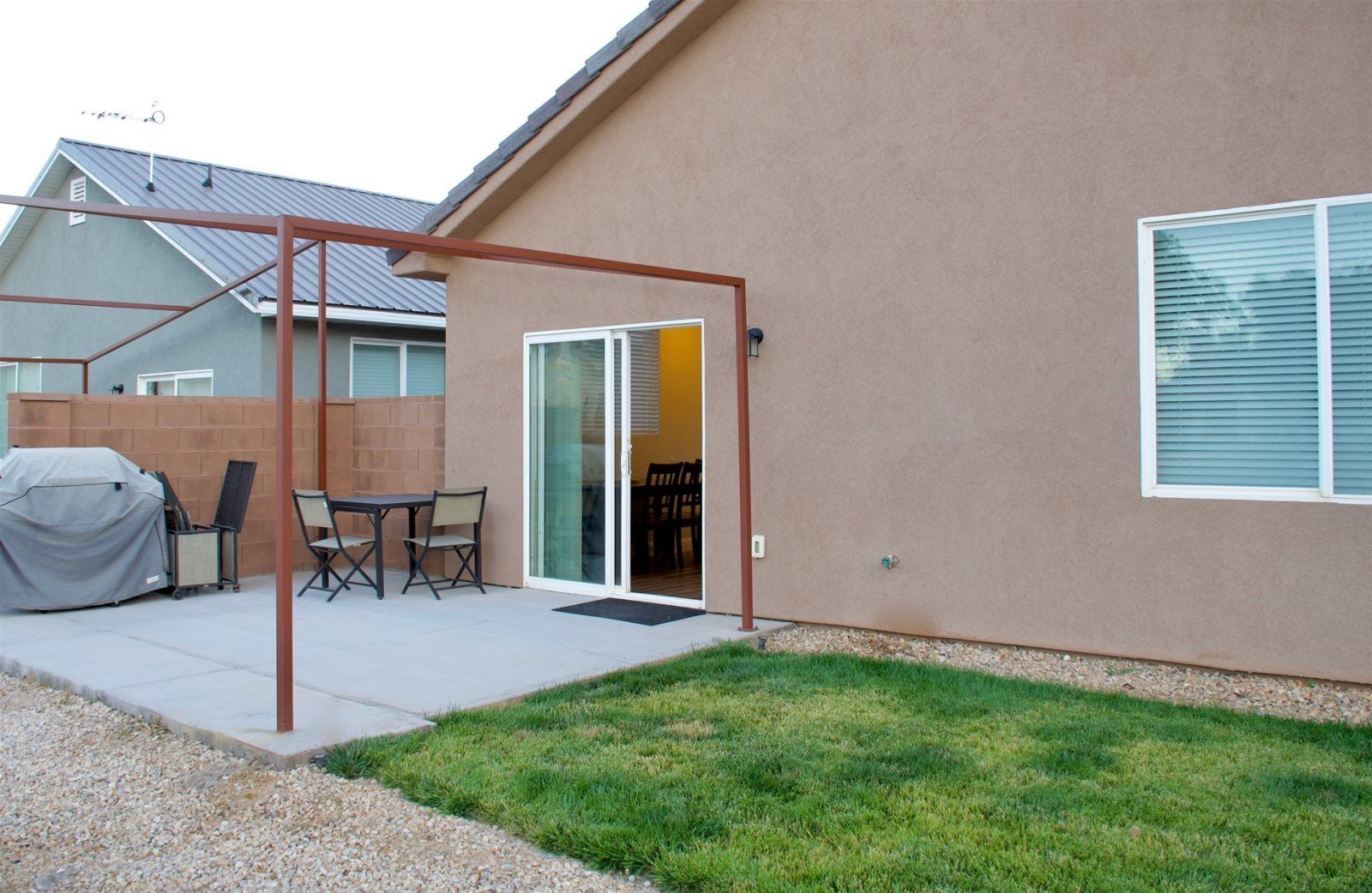 A patio area with a covered table and chairs, a sliding glass door leading to an interior space, and a small lawn.