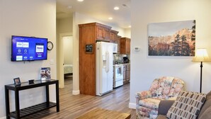 A living room with a television, a coffee table, a floral armchair, and a painting of a mountain landscape. - Zion's Camp and Cottages (La Verkin)
