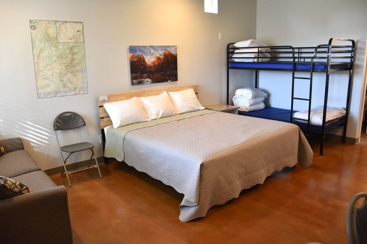 A room with a bunk bed, a single bed, a chair, a map on the wall, and a painting.