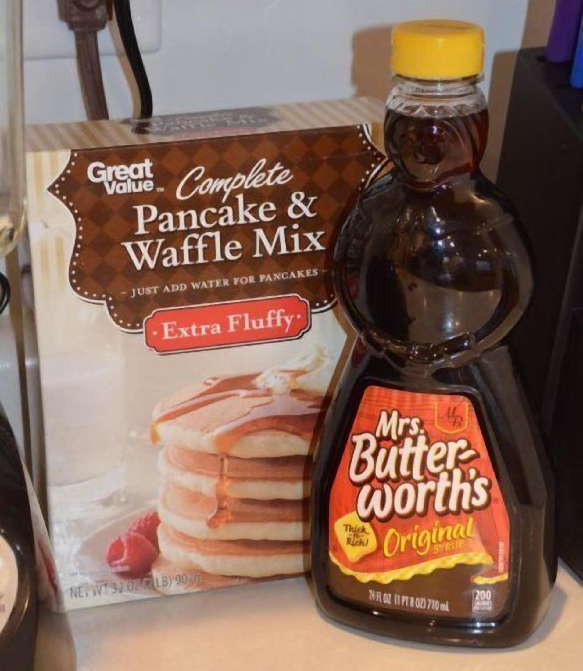 Eine Packung Great Value Complete Pancake & Waffle Mix und eine Flasche Mrs. Butterworth's Original Sirup auf einer Küchenarbeitsplatte.