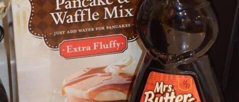 Eine Packung Great Value Complete Pancake & Waffle Mix und eine Flasche Mrs. Butterworth's Original Sirup auf einer Küchenarbeitsplatte.