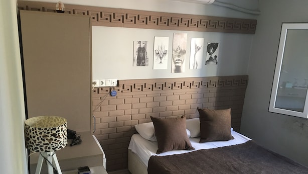 A bedroom with a brick-patterned headboard, a bed with brown bedding, a desk with a lamp, and artwork on the wall. - Asus Palmiye Otel (Adana)