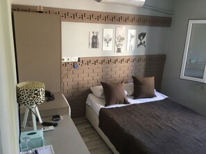 Een slaapkamer met een hoofdbord met een baksteenpatroon, een bed met bruin beddengoed, een bureau met een lamp en kunst aan de muur.