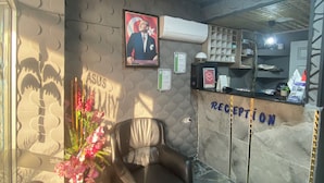 A reception area with a reception desk, two leather chairs, a wall with a framed picture, and a ceiling with a patterned design. - Asus Palmiye Otel (Adana)