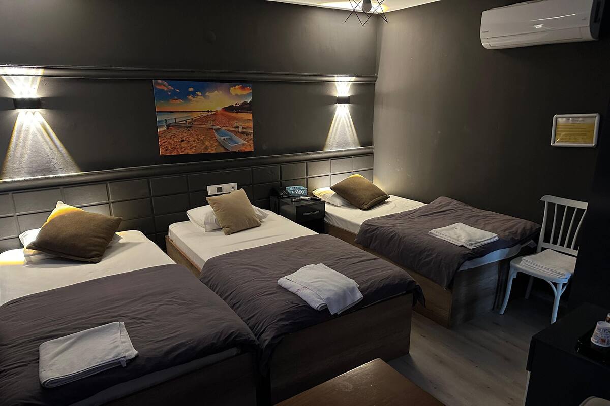 A hotel room with three beds, a desk, a chair, and a painting on the wall.