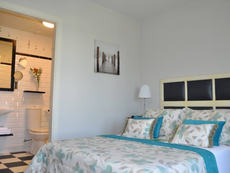 Ein Schlafzimmer mit Bett, Nachttisch, Lampe, einem Wandbild und einem Badezimmer mit Waschbecken und Toilette.