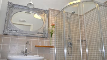 A bathroom with a white sink, a mirror with an ornate frame, a shower with a glass door, and a vase with flowers on the counter.