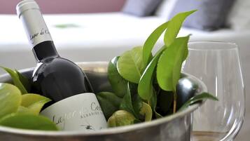 A bottle of wine and a glass in a metal container, surrounded by green leaves.