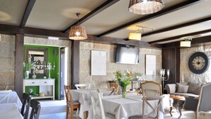 A dining area with tables set for two, a television mounted on the wall, and a clock.