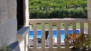 A stone balcony with a view of a vineyard and a pool.