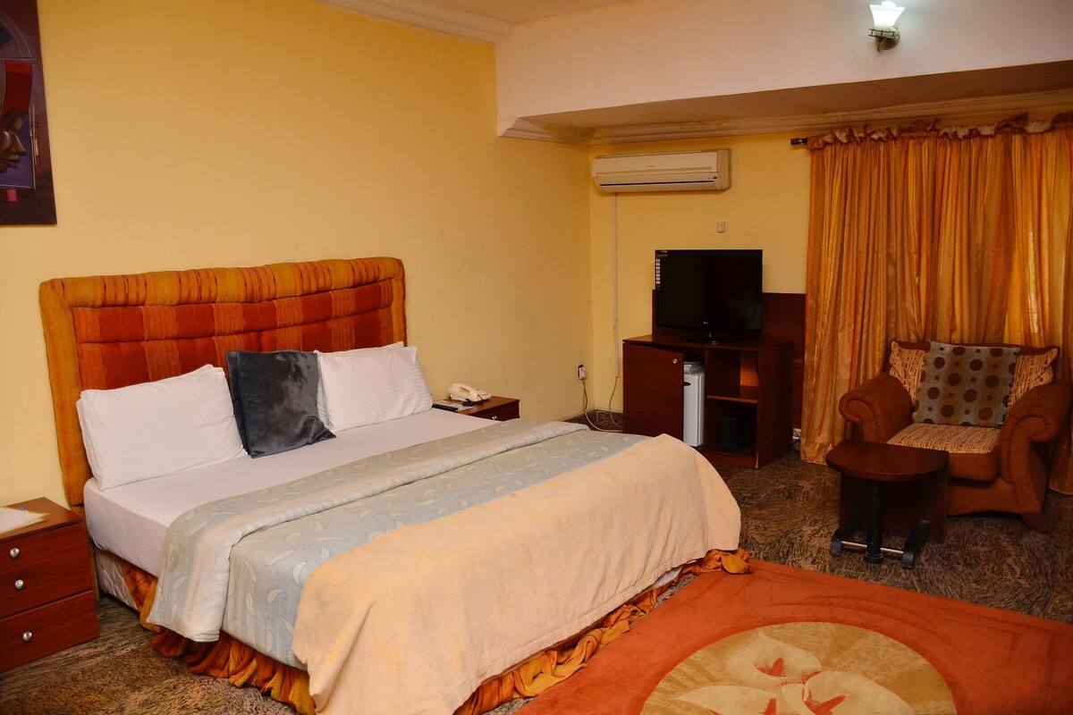 Habitación de hotel con una cama, televisor, una silla y unidad de aire acondicionado.