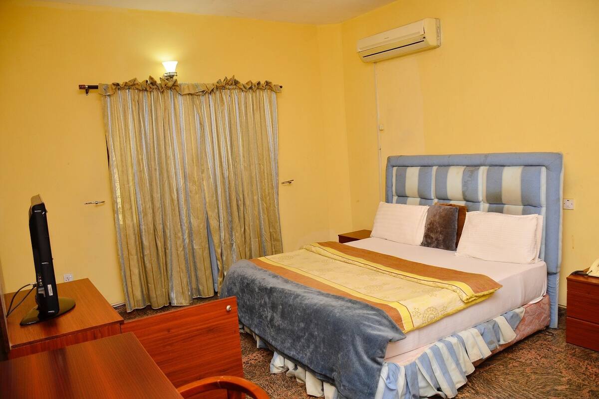Una habitación de hotel con cama, escritorio, aire acondicionado y cortinas.