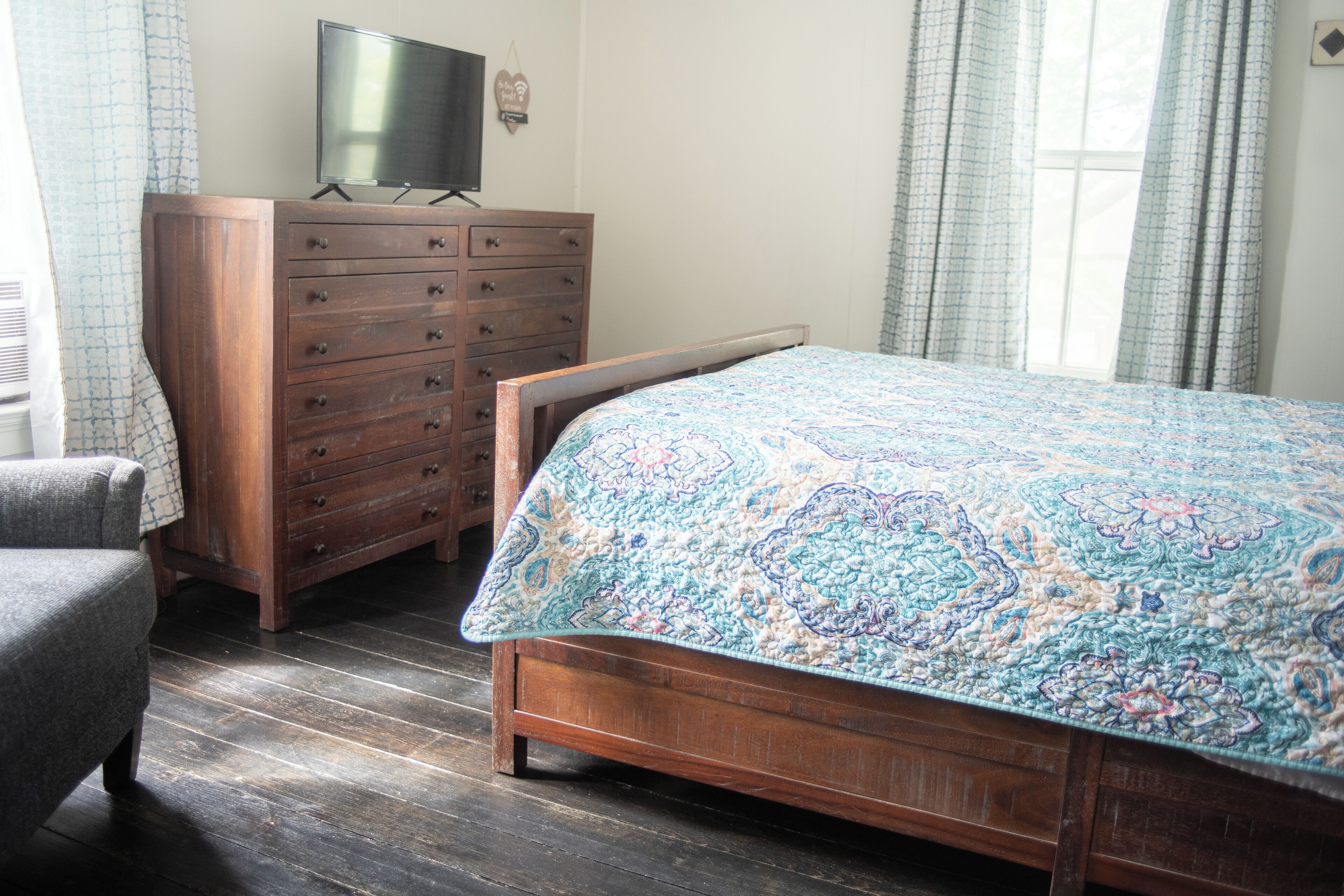 A bedroom with a wooden bed, a dresser, a television on top, and a chair.