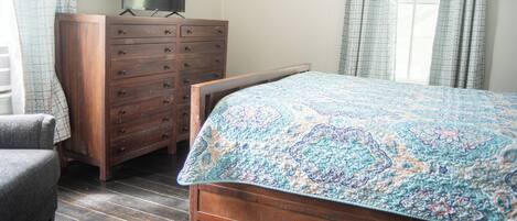 A bedroom with a wooden bed, a dresser, a television on top, and a chair.