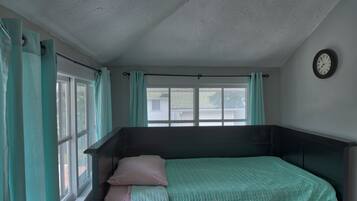 A small, single-bed room with a window, curtains, and a wall clock.