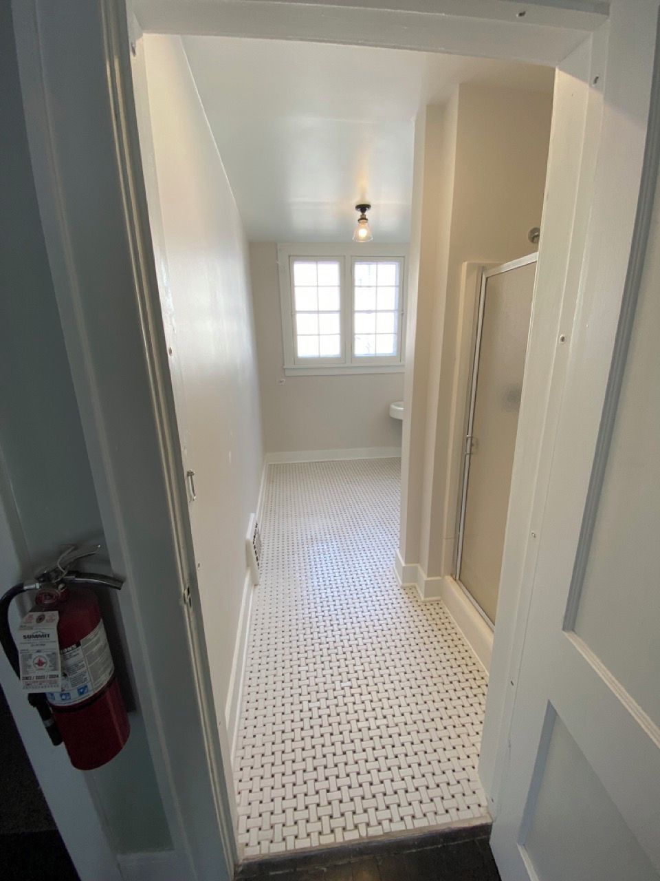 A narrow hallway with a patterned floor, a fire extinguisher on the left, and a door on the right.