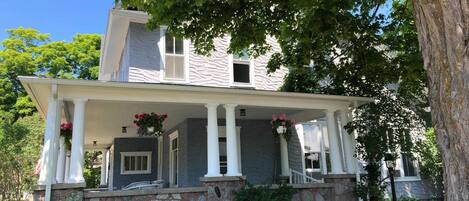 A two-story house with a stone foundation, a porch with white columns, and hanging flower baskets.