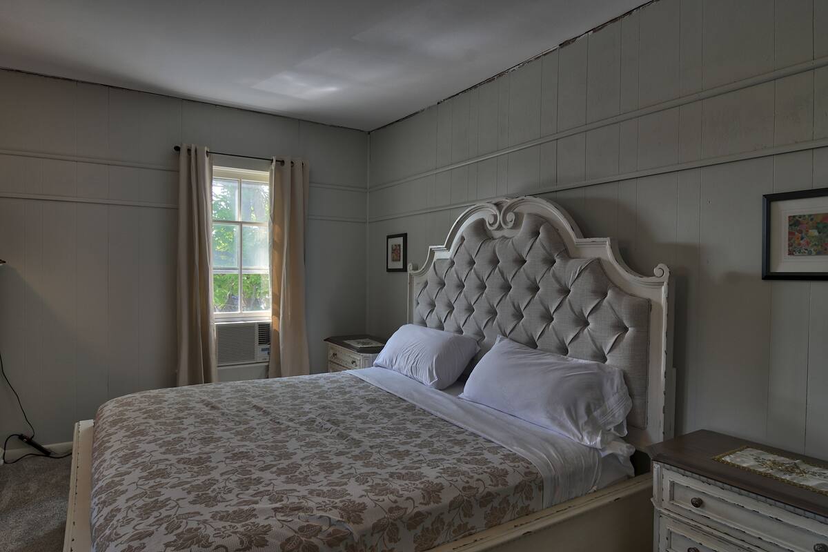 A bedroom with a large bed, a nightstand, a dresser, and a window with curtains.